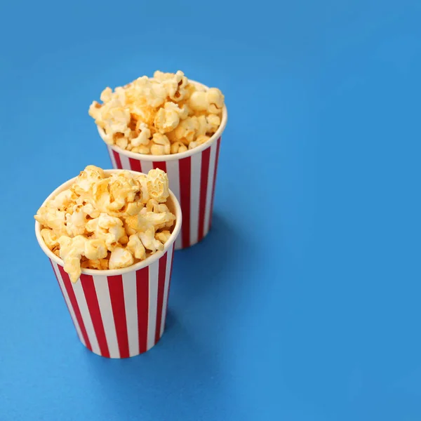 Dos tazas de papel blanco y rojo a rayas con palomitas de maíz crujientes fragantes se destacan una tras otra sobre un fondo azul claro, espacio para copiar, primer plano, cuadrado — Foto de Stock