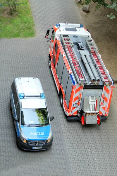 Carro de polícia azul claro fica ao lado de um caminhão de bombeiros vermelho brilhante com uma inscrição em língua alemã Frankfurt Fire Service — Fotografia de Stock