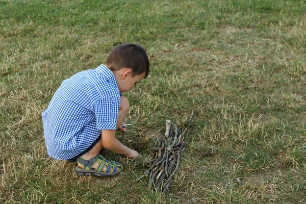 Chłopiec w koszuli buduje tratwę oddziałów w parku — Zdjęcie stockowe