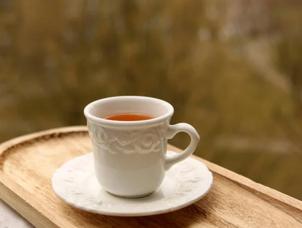 Чай в белой чашке с блюдцем стоит на светлой доске на фоне зелени — стоковое фото