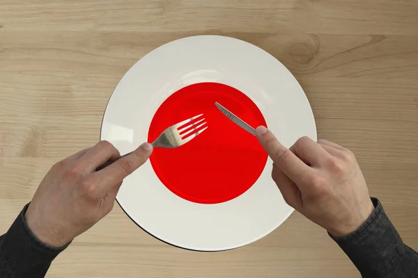 Руки со столовыми приборами на тарелке с государственным флагом Японии, копировальное место — стоковое фото