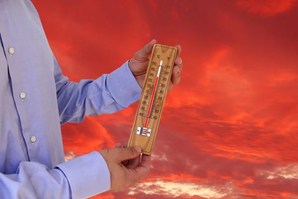 Die Hand des Mannes im Hemd hält ein Thermometer, das die Temperatur misst, das Konzept der Hitze, des Klimawandels, der globalen Erwärmung, 30 Grad Celsius, 83 Grad Fahrenheit vor einem feuerroten Himmel. — Stockfoto