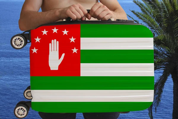 Tourist hält mit zwei Händen einen Koffer mit der Nationalflagge der abchasischen, nicht anerkannten georgischen Republik, ein Symbol für Urlaub, Einwanderung — Stockfoto