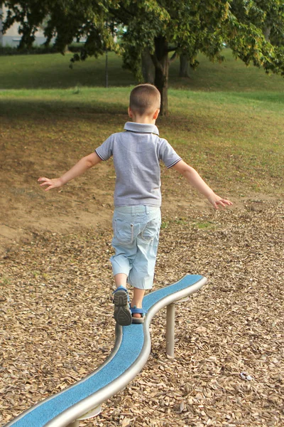 Niño preescolar en pantalones cortos camina en proyectil de juegos deportivos horizontales en el patio de recreo en el parque en verano, coordinación de entrenamiento y equilibrio corporal —  Fotos de Stock