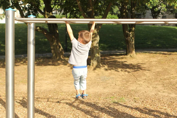 Boy förskolebarn klättrar en sportspel projektil på lekplatsen i parken på sommaren, utbildning hans händer och smidighet — Stockfoto