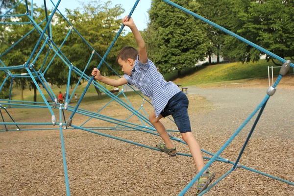 Boy skolpojke klättrar en sportspel projektil på lekplatsen i parken på sommaren, utbildning hans händer och smidighet — Stockfoto