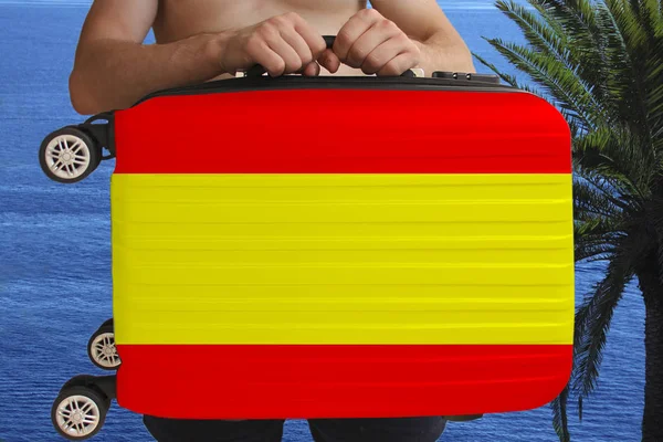 Турист держит двумя руками чемодан с национальным флагом Испании, символ туризма, иммиграции, политического убежища — стоковое фото