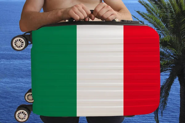 Турист держит с двумя руками чемодан с национальным флагом Италии, символом туризма, иммиграции, политического убежища — стоковое фото