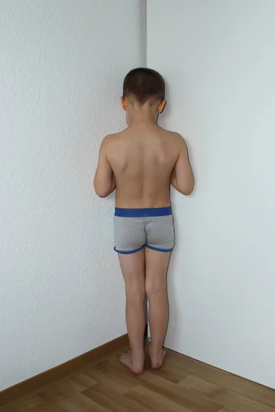 boy, junior schoolboy, standing in the corner undressed, facing the wall, punished by his parents for offense, parenting concept