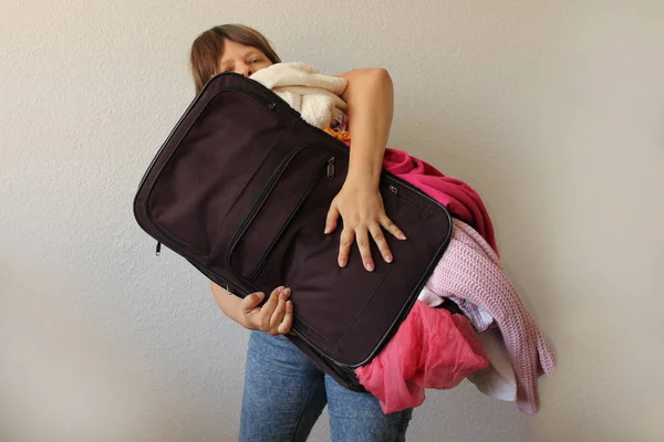 Femme tient une valise bondée, à partir de laquelle les choses tombent, concept de vacances, Voyage, tourisme — Photo