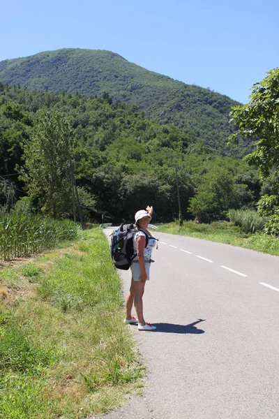 Женщина в шортах с большим туристическим рюкзаком на спине идет по дороге в горы — стоковое фото