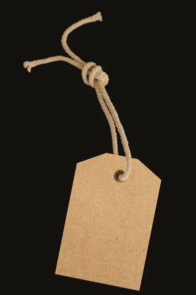 Etiqueta de preço de papel em branco ou etiqueta em um belo cordão torcido, isolado em um fundo preto — Fotografia de Stock