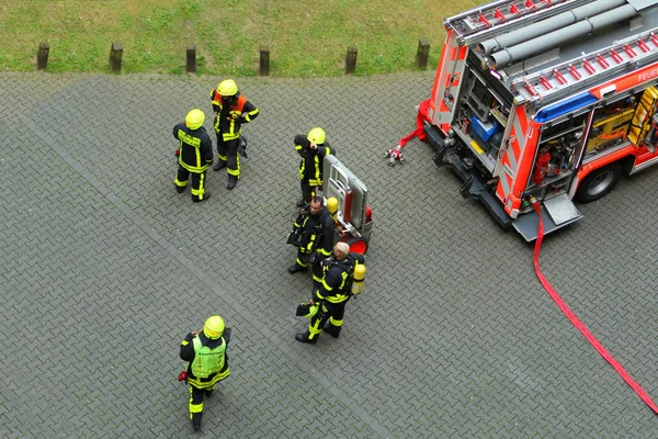 Франкфурт, Германия, июнь 2019: команда пожарных в ярко-желтой форме стоит возле ярко-красной пожарной машины — стоковое фото