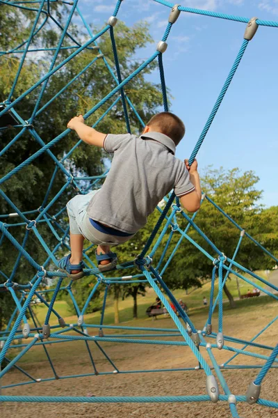 Boy förskolebarn klättrar en sportspel projektil på lekplatsen i parken på sommaren, utbildning hans händer och smidighet — Stockfoto