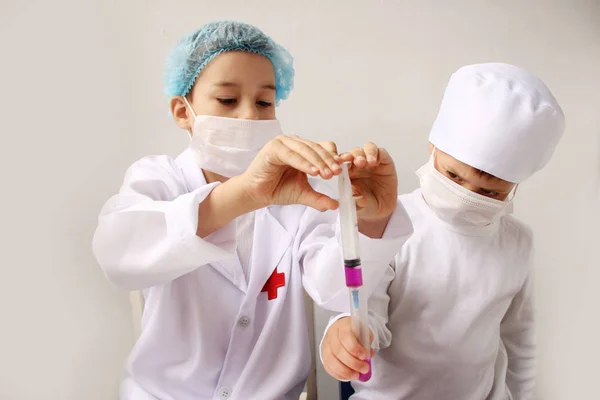 Два мальчика в белой медицинской форме в защитных масках и шапках проводят химические эксперименты в лаборатории — стоковое фото