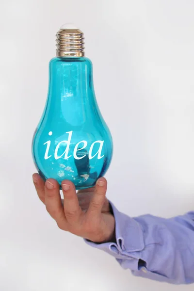 Businessman in a blue shirt holds in his hand a big blue glass lamp with the inscription idea, the concept of electricity, the idea, copy space — Stock Photo, Image