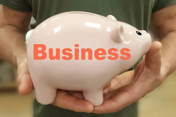 Grote roze Keramische Piggy Bank met het inscriptionsymbool van zakelijke kleur levend koraal in de handen van een man, close-up, concept van sparen en accumuleren van geld — Stockfoto