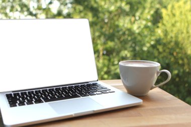 Açık bir kafede ahşap bir masada bir fincan kahve ile boş beyaz masaüstü ekranlı bir dizüstü bilgisayar kullanarak keyifli bir sabah görüntü alay