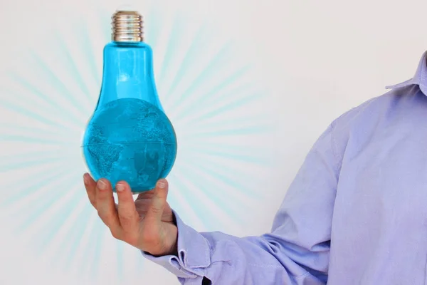 Biznesmen w niebieskiej koszulce trzyma w ręku wielką niebieską szklaną lampę z modelem planety Ziemia, pojęcie energii elektrycznej, ekologia, idea, przestrzeń kopiowania — Zdjęcie stockowe