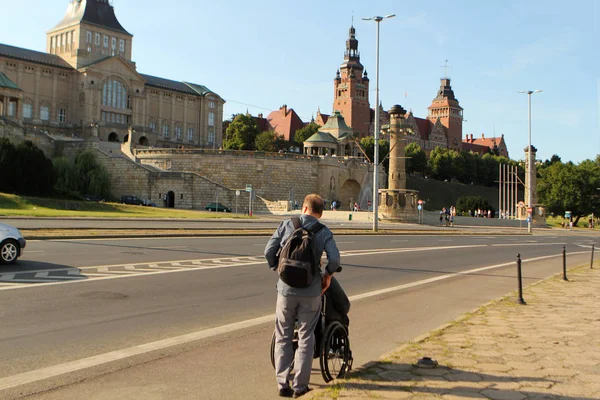 Szczecin, Polônia - julho de 2019: um homem carrega uma pessoa com deficiência em um carrinho no dique de Vala Brave — Fotografia de Stock