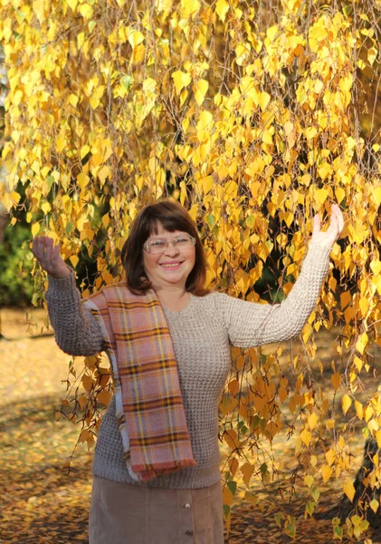 女性は美しいオレンジ色の秋の風景、公園の木々、クローズアップを背景に秋の公園で白樺のそばに立っています — ストック写真