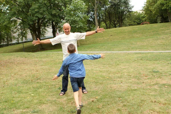 Homem e menino correm um para o outro, de braços abertos, no parque de verão, conceito de família — Fotografia de Stock