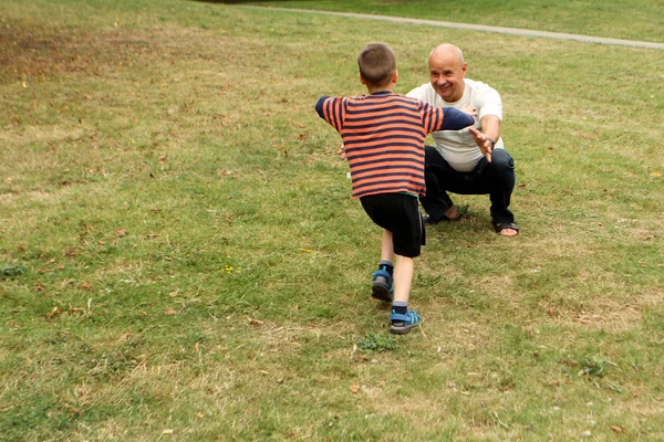 Niño, preescolar, estudiante de primaria se encuentra con los brazos del abuelo, un hombre mayor, en el parque, el concepto de relaciones familiares — Foto de Stock