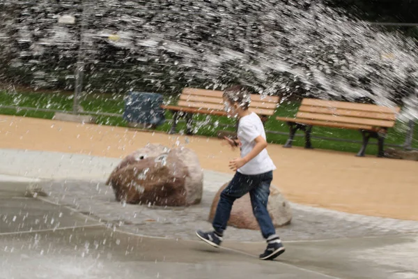 The boy runs under a large stream of water with spray — Stock Photo, Image