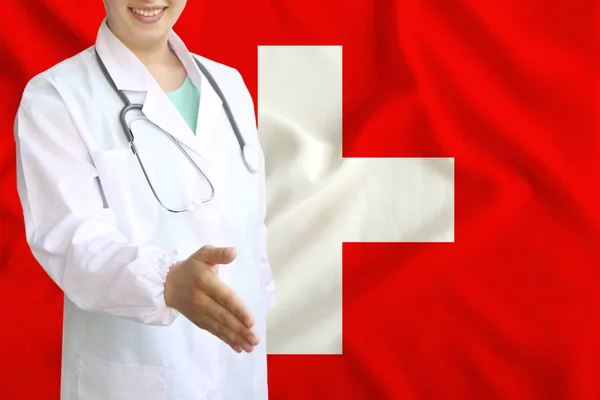 Junge schöne Ärztin mit einem offenen Lächeln reicht seine Hand zur Begrüßung auf dem Hintergrund der Nationalflagge, Konzepte des Gesundheitswesens, der Medizin — Stockfoto