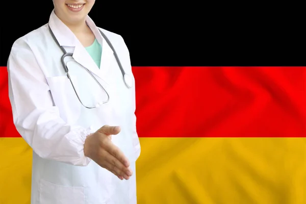 Joven hermosa niña médico con una sonrisa abierta extiende su mano para saludar en el fondo de la bandera nacional, conceptos de salud, medicina —  Fotos de Stock