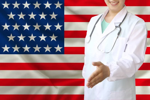 Junge schöne Ärztin mit einem offenen Lächeln reicht seine Hand zur Begrüßung auf dem Hintergrund der Nationalflagge, Konzepte des Gesundheitswesens, der Medizin — Stockfoto