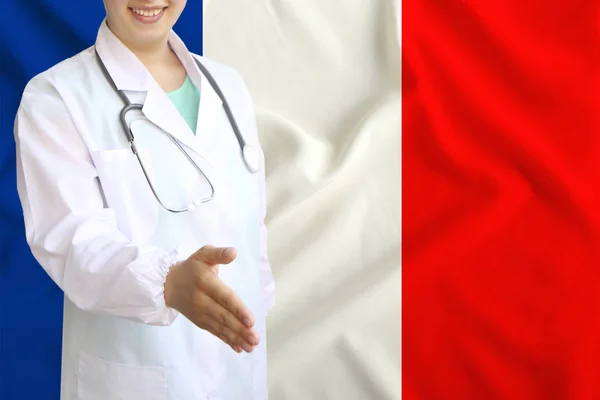 Mladá krásná dívka lékař s otevřeným úsměvem vztáhne ruku na pozdrav na pozadí národní vlajky, pojmy zdravotní péče, medicína — Stock fotografie