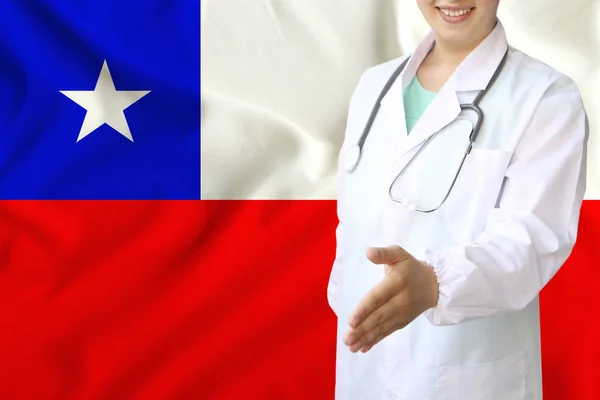 Fiatal gyönyörű lány orvos nyitott mosollyal kinyújtja a kezét üdvözlésére hátterében a nemzeti zászló, fogalmak egészségügyi ellátás, orvostudomány — Stock Fotó