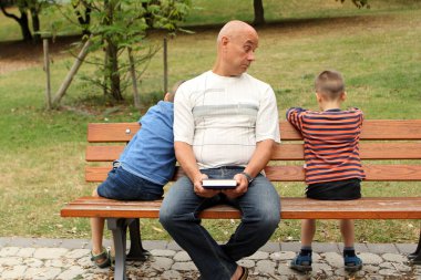 erkek, okul öncesi, ilkokul öğrencisi bir kitap ile dedesi yanında parkta bir bankta oturuyor, okumak istemiyorum, döndü, kuşaklar arası aile ilişkileri kavramı