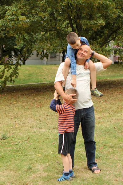 Muž, dědeček jemně objal svého vnuka, na ramenou mu seděl druhý chlapec, v letním parku, rodinná koncepce — Stock fotografie