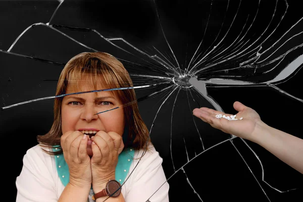 Pretty middle-aged woman with a grimace of stress and despair bites clenched hands, black background of broken glass, female hand holds out a handful of white pills, close-up, copy space — Stock Photo, Image