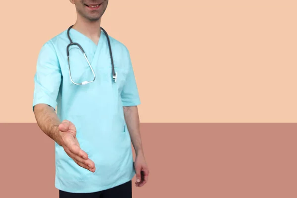 Boynunda bir stetoskop ile mavi üniformalı profesyonel giysiler erkek doktor renkli bir arka plan, tıbbi kavram, yakın çekim, kopya alanı tebrik için elini uzatır — Stok fotoğraf