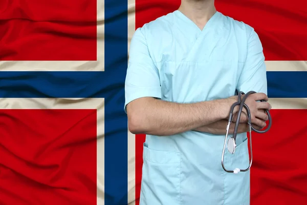 male doctor in uniform professional clothes with a stethoscope stands against the background of the national flag, the concept of the country\'s health and medical insurance, close-up, copy space