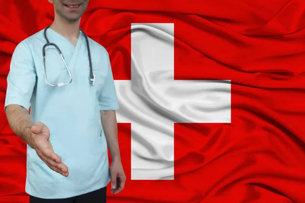 male doctor in uniform professional clothes with a stethoscope welcomes patients with his hand against the background of the national flag, the concept of the country\'s health and medical insurance