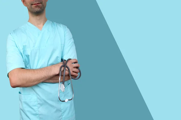 Mannelijke arts in blauw uniform met professionele kleren met een stethoscoop in handen op een gekleurde achtergrond, blauw, medisch concept, close-up, kopieer ruimte — Stockfoto