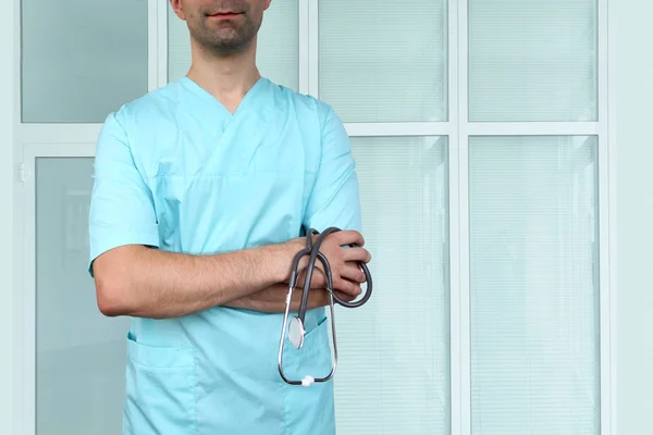 Mannelijke arts in blauw uniform met professionele kleren met een stethoscoop in handen op een gekleurde achtergrond van ziekenhuis interieurs, medisch concept, close-up, kopieer ruimte — Stockfoto