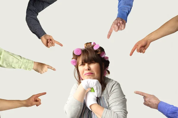 Mujer de mediana edad, una ama de casa con rizadores, con una expresión infeliz en su cara, se apoya en una fregona con ambas manos en guantes blancos, y desde todos los lados se muestra con los dedos —  Fotos de Stock