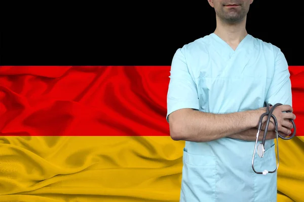 Male doctor in uniform professional clothes with a stethoscope stands against the background of the national flag, the concept of the country's health and medical insurance, close-up, copy space — Stock Photo, Image