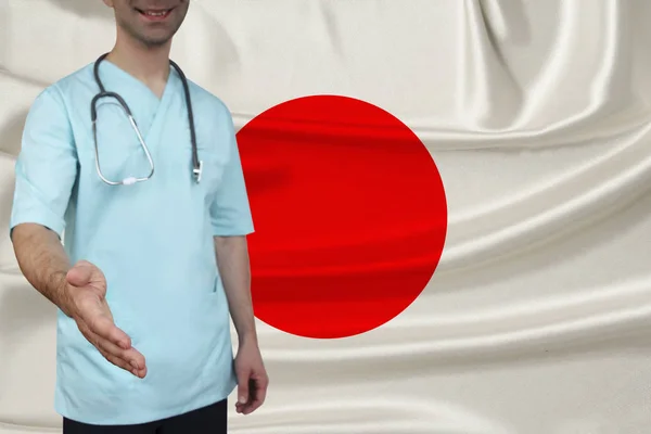 Mannelijke arts in uniforme professionele kleren met een stethoscoop verwelkomt patiënten met zijn hand tegen de achtergrond van de nationale vlag, het concept van de gezondheid van het land en de medische verzekering — Stockfoto