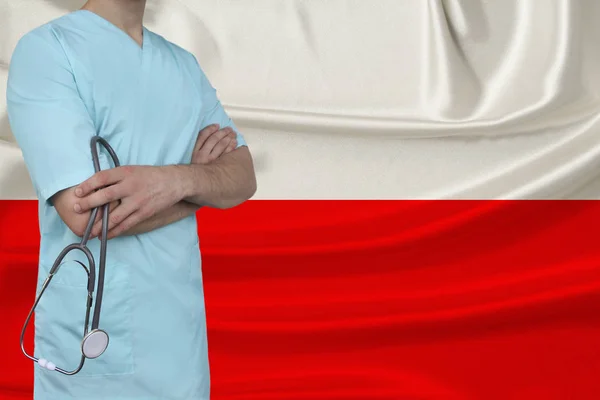 Mannelijke arts in uniform professionele kleding met een stethoscoop staat tegen de achtergrond van de nationale vlag, het concept van de gezondheidszorg en ziektekostenverzekering van het land, close-up, kopieerruimte — Stockfoto