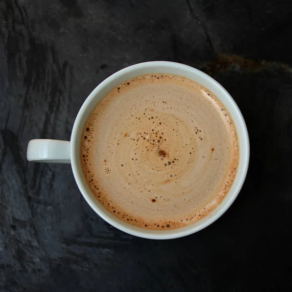 Witte beker met cappuccino en snoep op een steen zwarte gestreepte tafel, bovenaanzicht, close-up, kopieer ruimte — Stockfoto