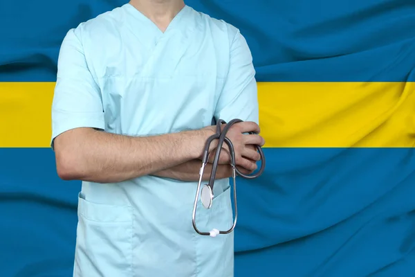 male doctor in uniform professional clothes with a stethoscope stands against the background of the national flag, the concept of the country\'s health and medical insurance, close-up, copy space