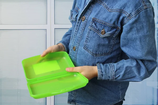 Colegial en una chaqueta de mezclilla lleva una lonchera de plástico vacía en las manos, un concepto de mala nutrición — Foto de Stock