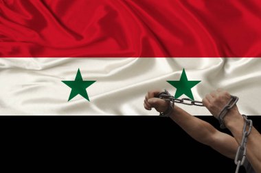 Suriye ulusal bayrağının arka planına karşı ağır demir zincirler halinde zincirlenmiş erkek kaba eller, ülkede suç kavramı, tutuklama, kanunsuzluk, baskı, yakın çekim, kopyalama alanı
