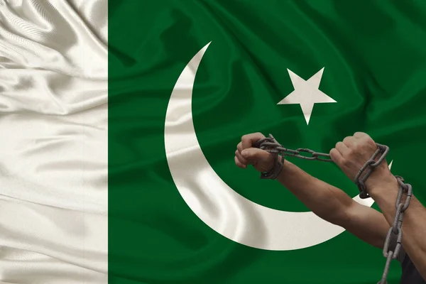 Manos gruesas masculinas encadenadas en pesadas cadenas de hierro en el trasfondo de la bandera nacional de Pakistán, el concepto de crimen en el país, arresto, ilegalidad, represión, primer plano, espacio para copiar — Foto de Stock